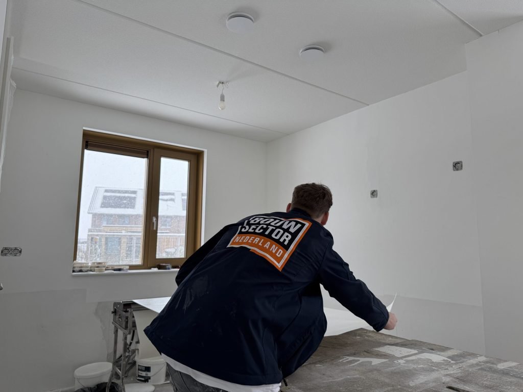 Vakman van Bouwsector Nederland legt een baan vlies op de plaktafel in een kale nieuwbouwkamer