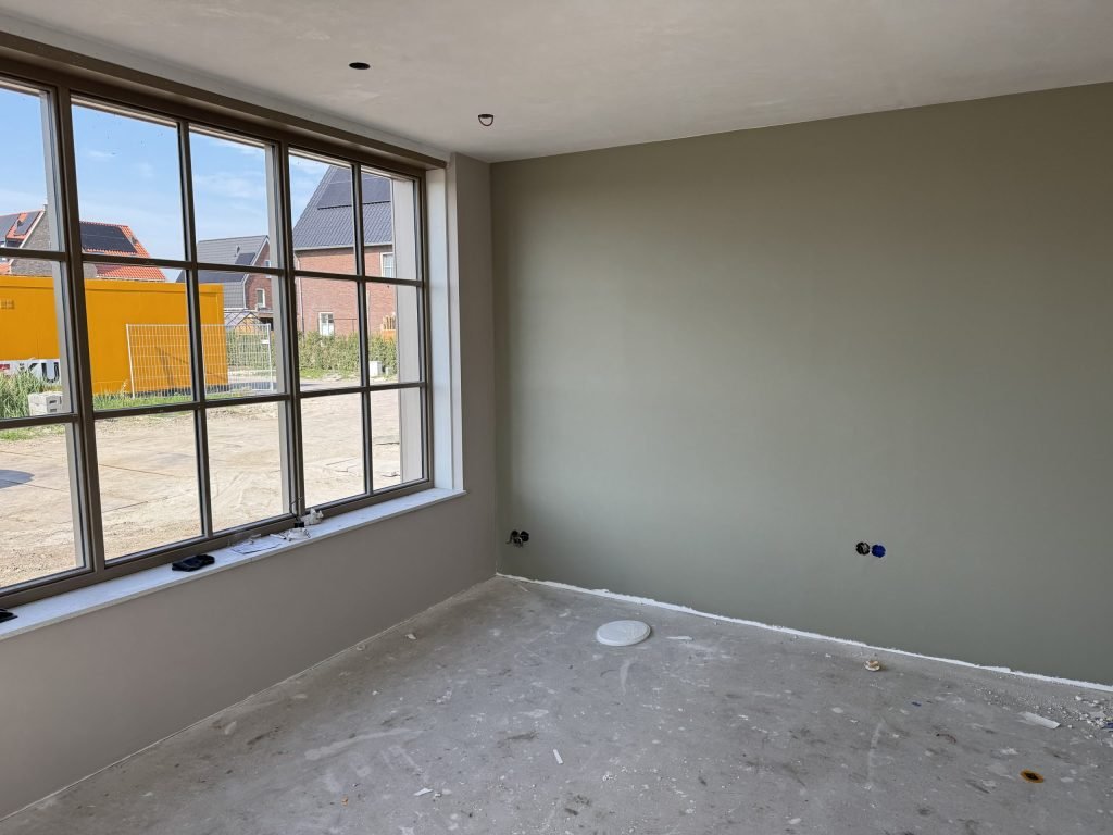 Nieuwbouwkamer met een egaal gesausde wand in een grijsgroene tint en een groot raam